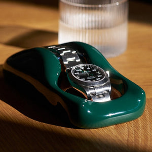 A British Racing Green watch holder with a Rolex Airking in it sitting on a desk