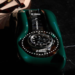 A British Racing Green watch holder with a Rolex Submariner in it sitting on a bedside table