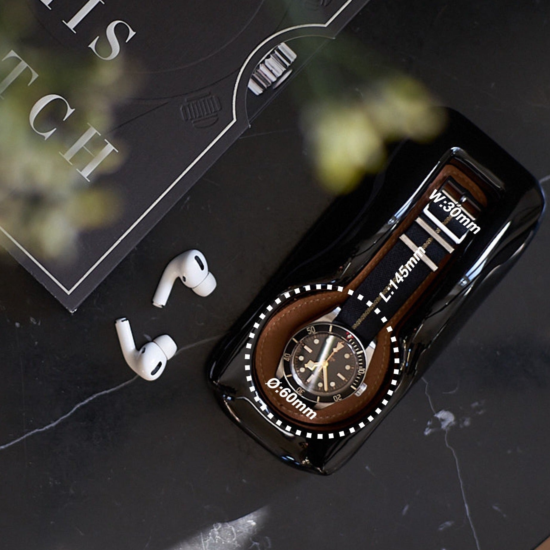 A watch holder with a Tudor Black 58 placed on a marble bedside table