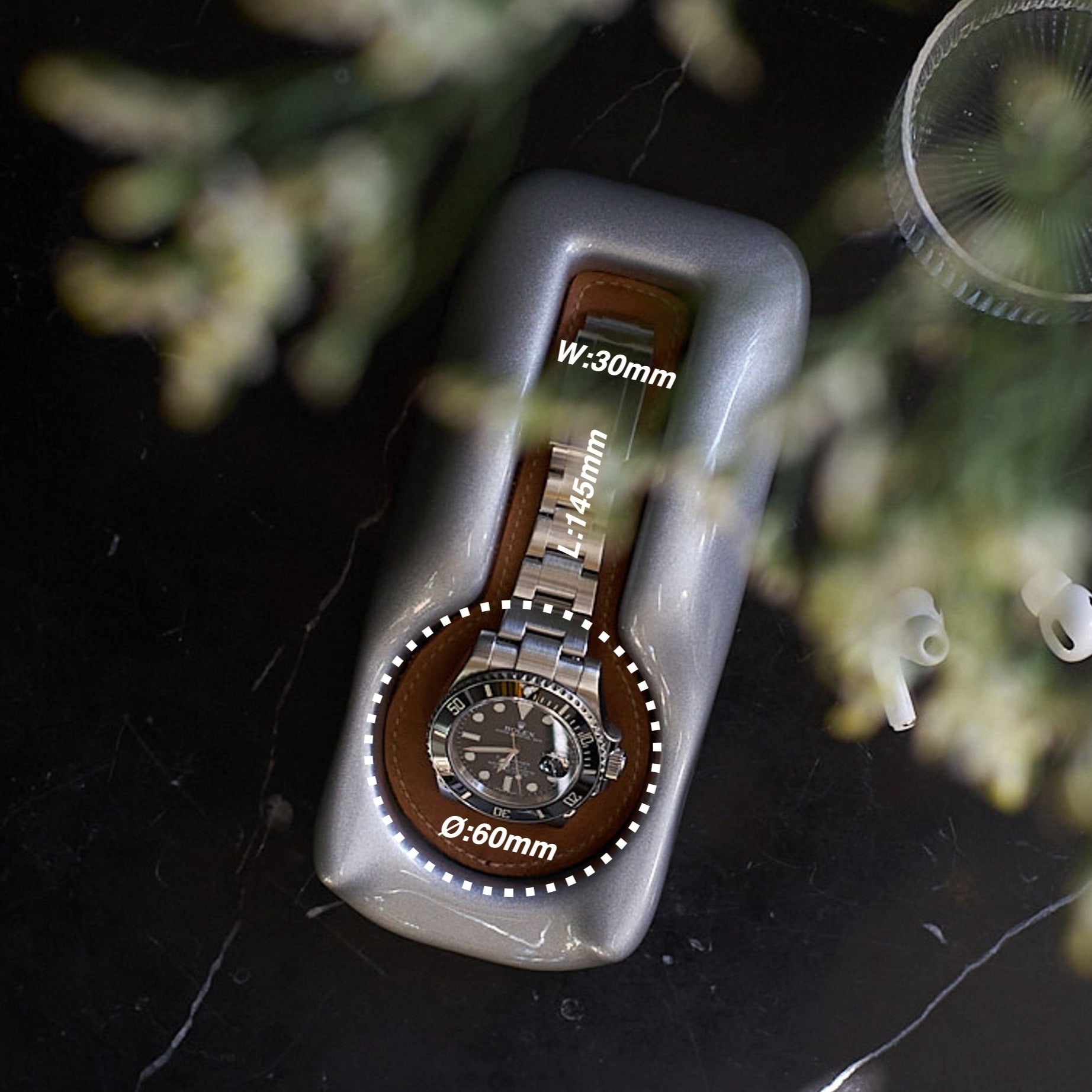 A Glacier Silver watch holder with a Rolex Submariner in it sitting on a marble bedside table